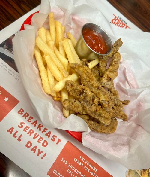 A basket of crispy fried chicken strips with a side of French fries and a small cup of dipping sauce.