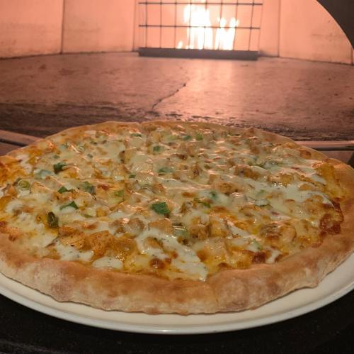 A freshly baked pizza with melted cheese and toppings, placed in front of a glowing wood-fired oven.