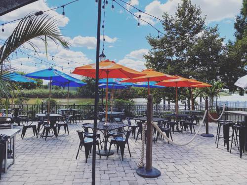 Outdoor dining area with colorful umbrellas, black tables, and a scenic view of trees and water under a blue sky.