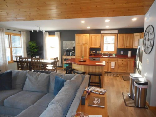 Cozy open-concept kitchen and living area with wooden accents, a large sofa, and a dining table. Bright and inviting atmosphere.
