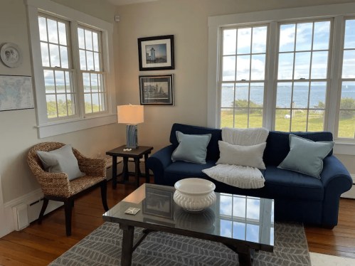 Cozy living room with a blue sofa, wicker chair, and large windows overlooking a scenic view of the water.