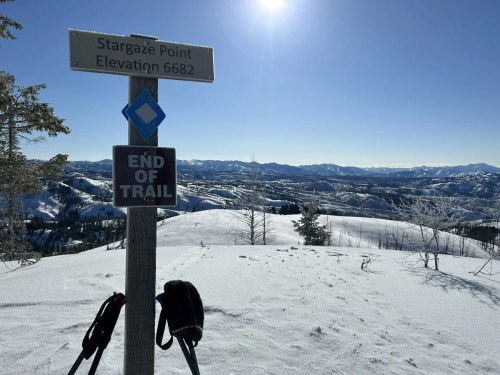 Signpost at Stargaze Point, elevation 6682 ft, with a snowy landscape and mountains in the background. End of trail marker visible.