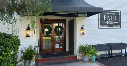 Entrance to the River Room, featuring double wooden doors, wreaths, and potted plants on either side.