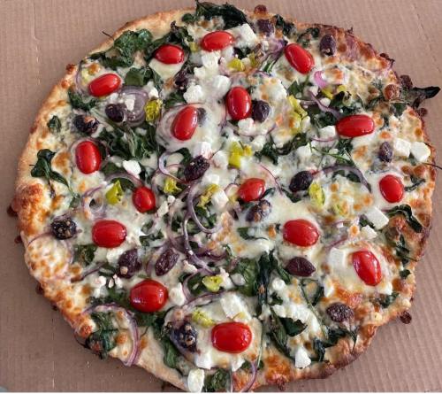 A freshly baked pizza topped with spinach, cherry tomatoes, olives, red onions, and feta cheese on a golden crust.