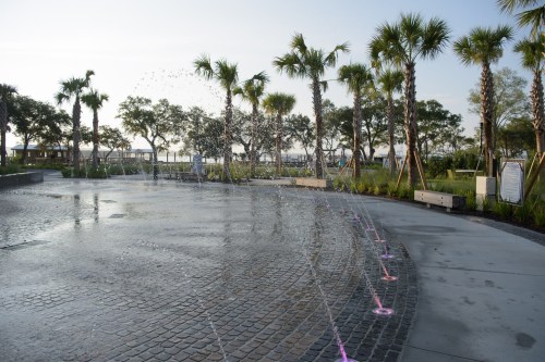 A scenic park with palm trees and a water fountain, featuring a cobblestone path and gentle morning light.