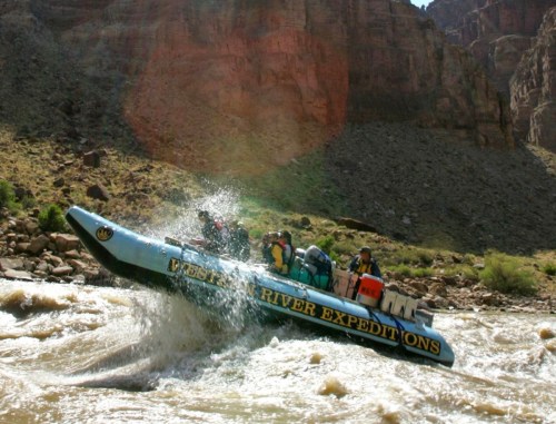 A blue raft splashes through whitewater rapids, with passengers enjoying an adventurous river expedition.