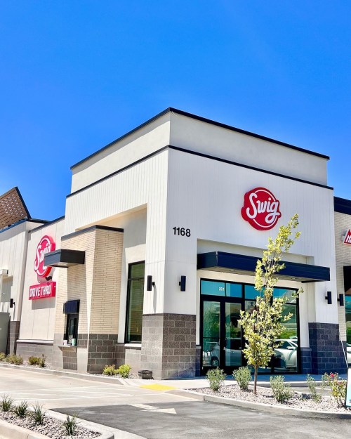 Exterior of a Swig restaurant with a bright blue sky, featuring a drive-thru and modern architectural design.