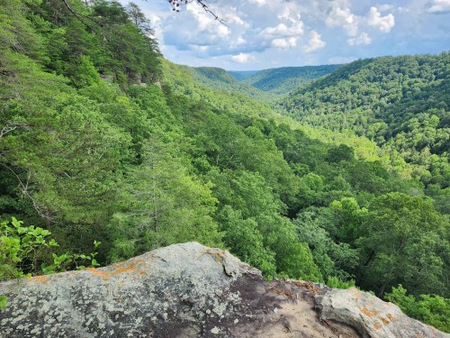 A scenic view of a lush green valley surrounded by hills under a partly cloudy sky.