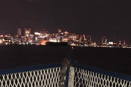 Night view of a city skyline illuminated with lights, seen from a boat on the water.