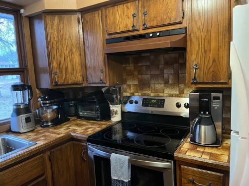 A cozy kitchen with wooden cabinets, an electric stove, and various appliances on the countertop.