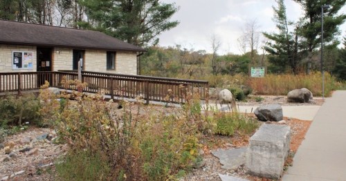 A small building with a wooden ramp, surrounded by rocks and greenery, set in a natural landscape.