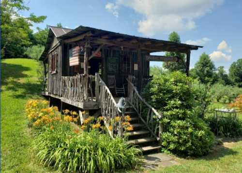 A rustic wooden cabin with a porch, surrounded by greenery and colorful flowers under a blue sky.