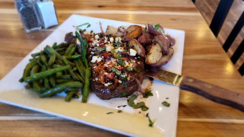 A plate featuring a grilled steak topped with herbs, served with green beans and roasted potatoes on a wooden table.