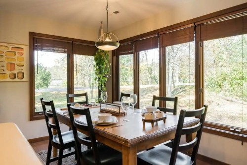 A cozy dining room with a wooden table, black chairs, and large windows overlooking a green landscape.