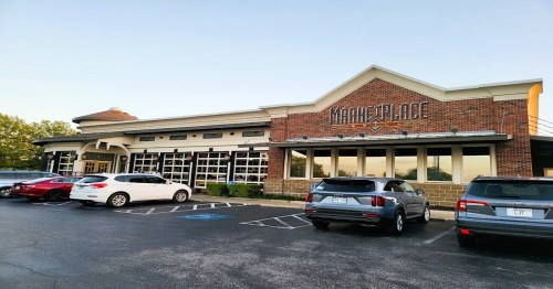 Exterior of a brick building labeled "Marketplace," with parked cars in front and a clear sky above.