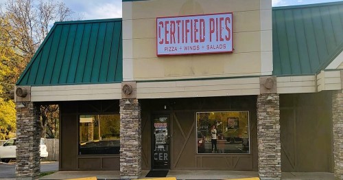 Exterior of a restaurant named "Certified Pies," featuring a green roof and stone accents, with large windows.