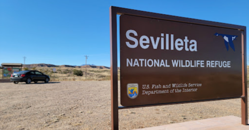 Sign for Sevilleta National Wildlife Refuge with a car parked nearby and a desert landscape in the background.