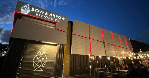 Exterior of Bow & Arrow Brewing Co. at night, featuring illuminated signage and string lights.