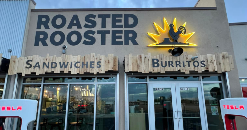 Exterior of Roasted Rooster restaurant featuring a sign with a rooster and neon accents, highlighting sandwiches and burritos.