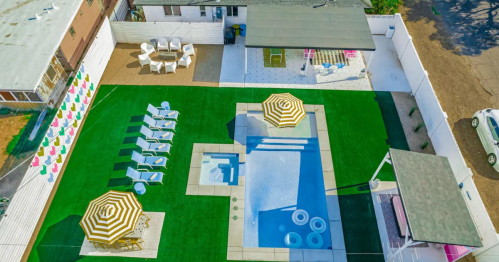 Aerial view of a backyard with a pool, lounge chairs, umbrellas, and seating areas on green grass.