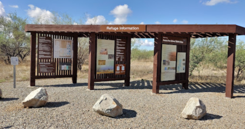 Information kiosk at a wildlife refuge, featuring multiple panels and surrounded by gravel and rocks.