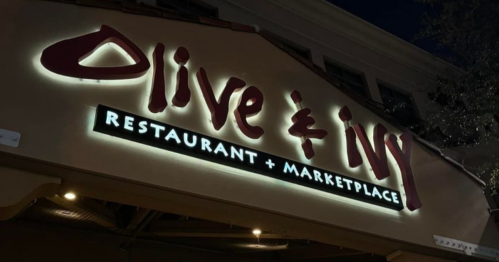 Sign for "Olive & Ivy Restaurant + Marketplace" illuminated at night.