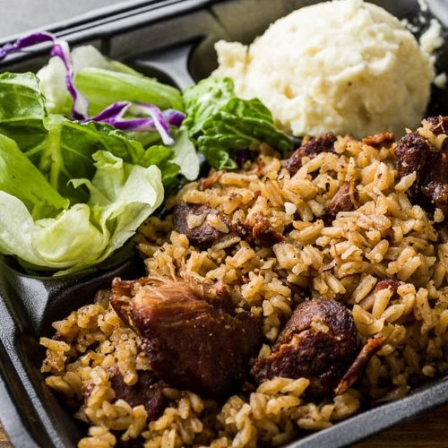 A black takeout container with rice, meat, mashed potatoes, and a side of lettuce and purple cabbage.