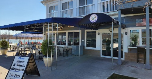 Exterior of a restaurant with a blue awning, outdoor seating, and a sign stating "Shoes & Shirts Required."