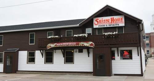 Exterior of Suisse Haus Food & Spirits, a two-story building with a brown and white facade and flower boxes.