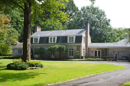 A charming stone house surrounded by lush greenery and a well-maintained lawn on a sunny day.
