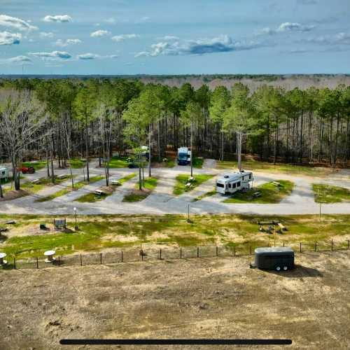 Aerial view of a campground with RVs parked among trees, surrounded by open grassy areas and a clear blue sky.