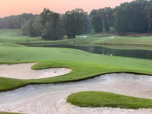 A serene golf course at sunrise, featuring lush green fairways, a pond, and sand traps.
