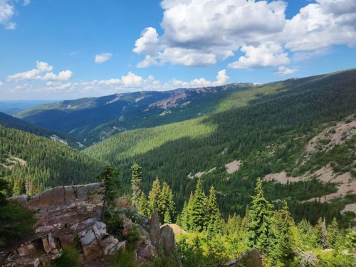 A panoramic view of lush green mountains under a blue sky with fluffy clouds, showcasing a serene natural landscape.