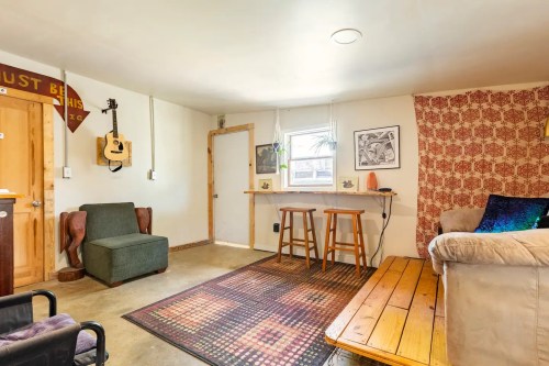 Cozy living space with a green chair, wooden table, and patterned wall, featuring natural light from a window.