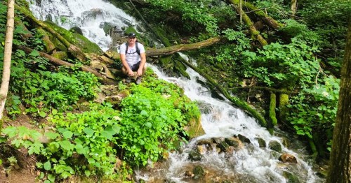 A hiker sitting on the rocky edges of a waterfall inside Leanord Springs, a hidden gem nature park in IN.