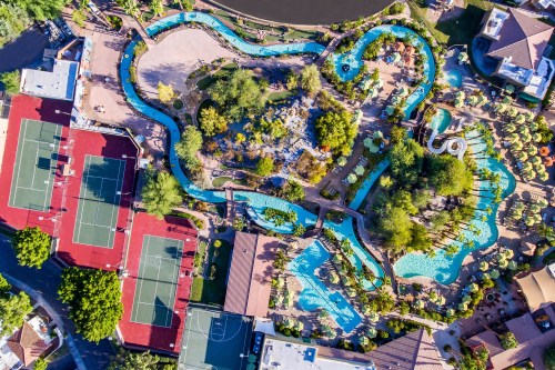 Aerial view of a resort featuring winding pools, lush landscaping, and tennis courts nearby.