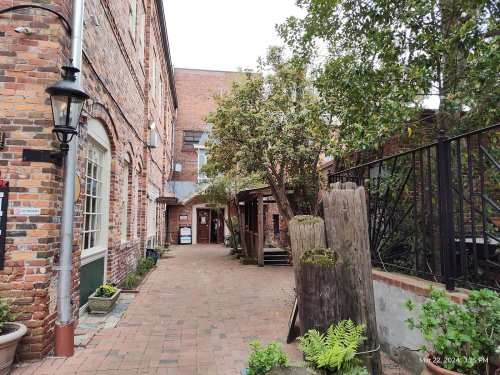 A brick pathway leads through a quaint courtyard with trees and rustic wooden features.