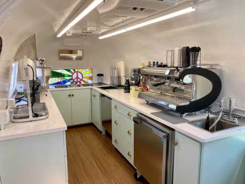 Interior of a modern coffee trailer with a sleek espresso machine, countertops, and colorful stained glass window.