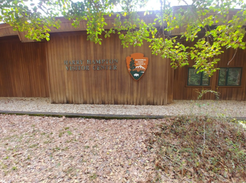 Exterior of the Harry Hampton Visitor Center, featuring wooden walls and a park service sign, surrounded by fallen leaves.