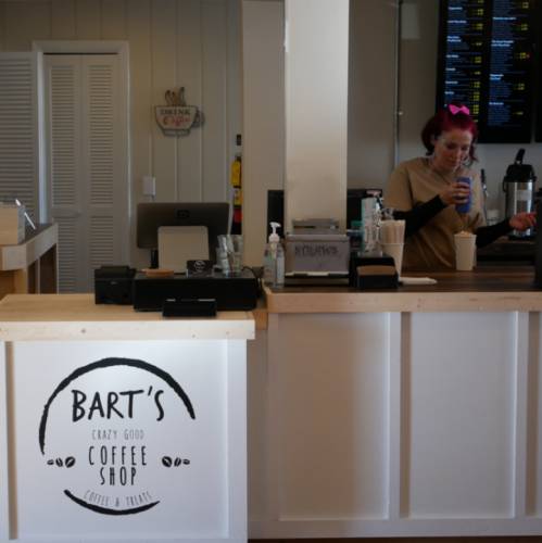 A coffee shop counter with a sign reading "Bart's Crazy Good Coffee Shop" and a barista preparing a drink.