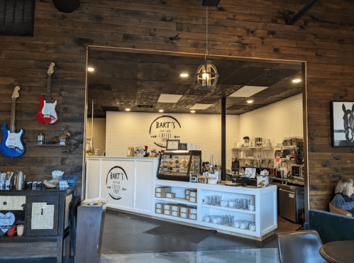 Cozy coffee shop interior with wooden walls, a counter, and guitars on display. Bright and inviting atmosphere.