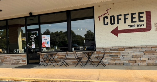 Exterior of a coffee shop with a sign reading "Great Coffee This Way" and outdoor seating.