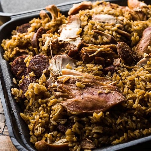 A close-up of a tray filled with flavorful rice mixed with pieces of chicken and sausage.
