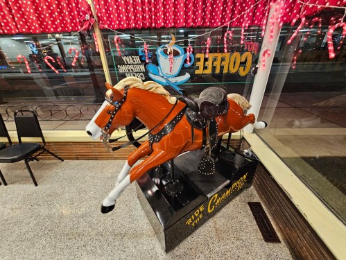 A vintage-style mechanical horse ride inside a café, with festive decorations and candy canes in the background.
