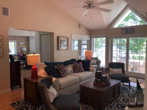 Cozy living room with a white sofa, decorative pillows, a wooden coffee table, and large windows overlooking a lake.