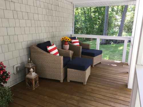 Cozy porch with two wicker chairs, blue cushions, decorative pillows, a vase of sunflowers, and a lantern.