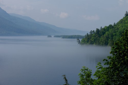 A serene lake surrounded by misty mountains and lush greenery, creating a tranquil and peaceful landscape.