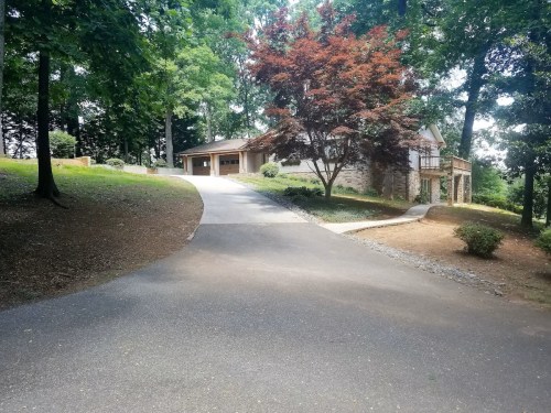 A winding driveway leads to a modern house surrounded by trees and greenery.