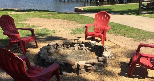 four red lawn chairs surrounding a rock pit near a lake