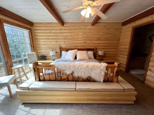 Cozy log cabin bedroom featuring a wooden bed with white bedding, a plush throw, and large windows for natural light.